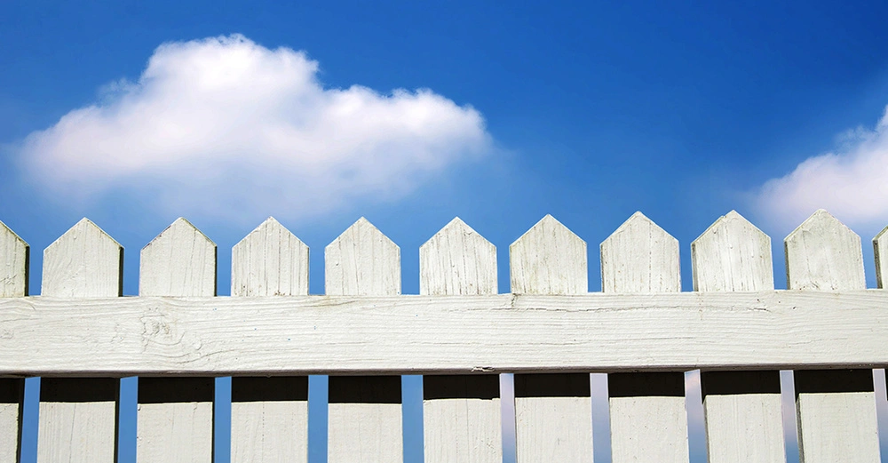 Weißer Lattenzaun im Garten unter blauen Himmel mit wenig Wolken.