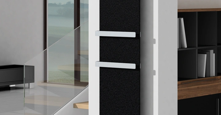 Schwarzer Heizkörper an der Wand montiert hält zwei weiße Handtuchhalter in einem modernen Raum mit heller Fliesenboden weiße Wände Glastreppen und großen Fenstern im Hintergrund.