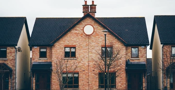 Backsteinhaus mit Spitzdach steht in einer Reihenhaussiedlung zwei kahle Bäume davor Laternenmast in der Mitte der ruhigen Straße. Keine identifizierbaren Personen oder Tiere sichtbar.