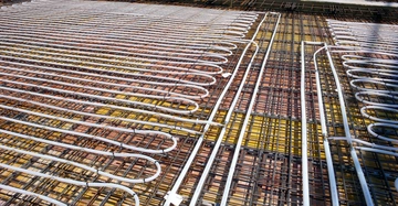 Betondecke mit weißen Heizschlangen der Bauteilaktivierung und sichtbarer Stahlbewehrung in rot-braun.