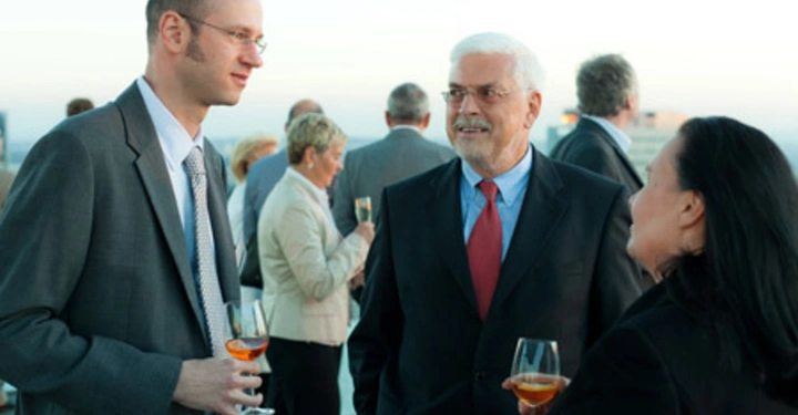 Galerie-Bild 31: Männer und Frauen in formeller Kleidung halten Gläser mit Getränken und unterhalten sich auf einer Dachterrasse bei Tageslicht im Freien. Mehrere Personen im Hintergrund sprechen ebenfalls.