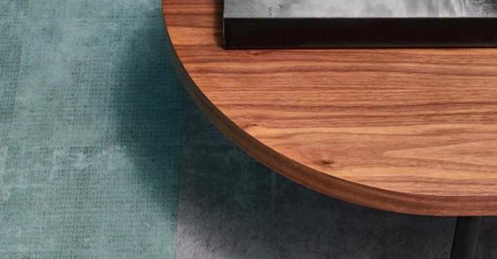 Runder Holztisch hält ein leuchtendes Glaslicht und ein Buch mit Regenschirmmotiv liegendem Boden grau-türkis.