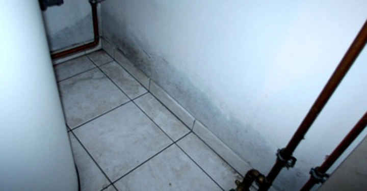 Galerie-Bild 2: Röhren verlaufen entlang einer Wand mit Fliesen auf dem Boden. Ein Wasserkocher befindet sich links. Der Boden und die Wand scheinen feucht oder leicht verschimmelt zu sein.