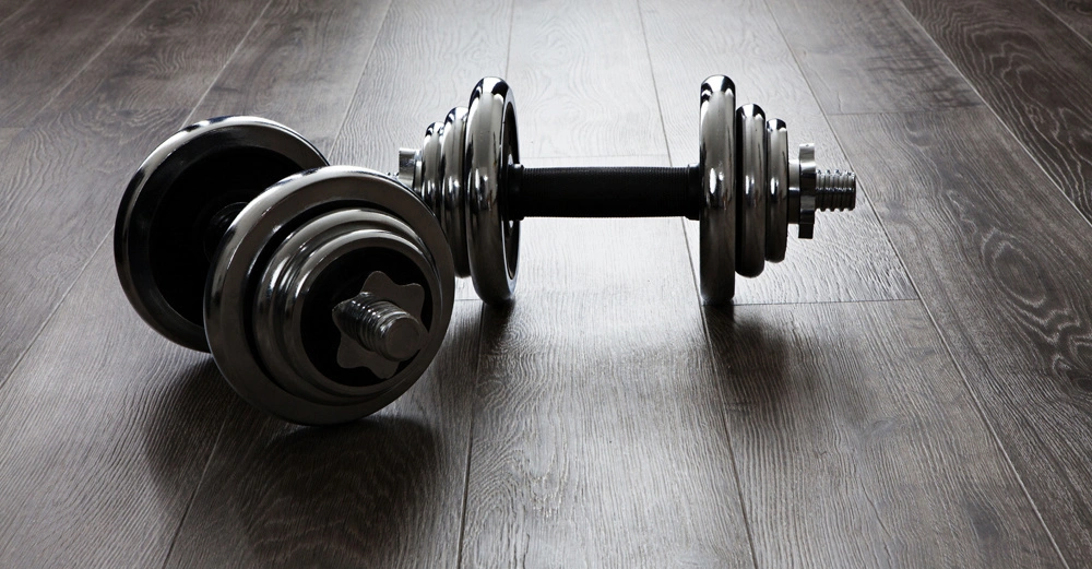 Hanteln liegen auf einem dunklen Holzboden in einem Innenraum.