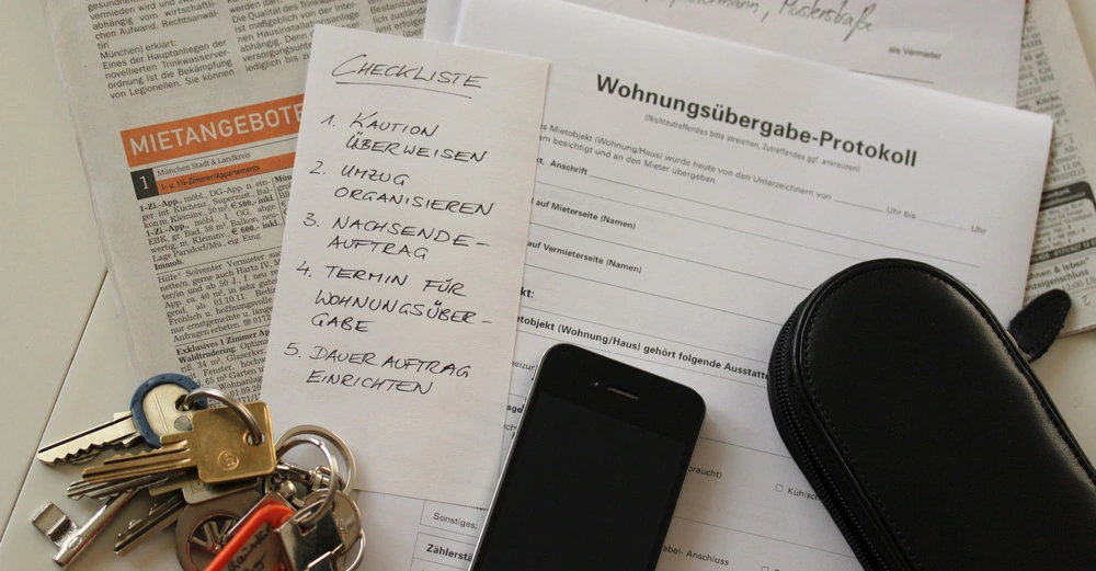 auf Tisch liegt eine Zeitung, Schlüsselbund, Notizzettel und ein Formular mit Titel Wohnungsübergabe zum Ausfüllen