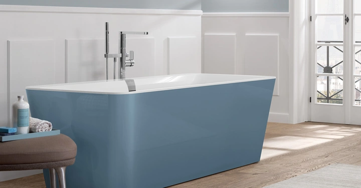 Blau-weiße freistehende Badewanne steht in einem eleganten Badezimmer mit Holzboden helblauen Wänden und weißen Verkleidungen durch große Türen fällt Tageslicht ein.