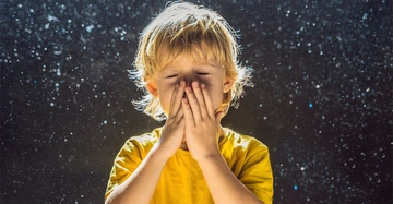 kleiner blonder Junge steht inmitten von fliegendem Staub und muss stark niesen.