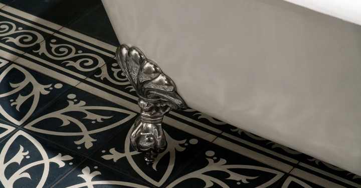Galerie-Bild 10: Ein verziertes Metallfußbein stützt eine weiße Badewanne auf kunstvoll gefliesten Bodenfliesen mit schwarzen und weißen Mustern.