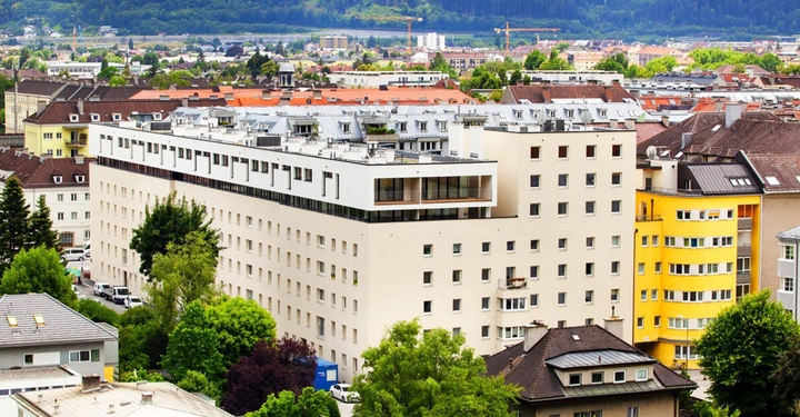 Galerie-Bild 3: Ein großes mehrstöckiges Wohngebäude steht mitten in einer Stadtlandschaft umgeben von anderen Häusern im Hintergrund sind Bäume und Hügel zu sehen.