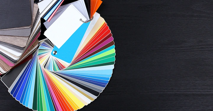 Farbmusterkarten-Fächer zeigt eine große Auswahl an Farben und Texturen auf einem dunklen Holztisch verstreut.