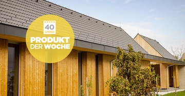 Gebäude mit Holzverkleidung steht still in einem Außenbereich mit Bäumen und Blauem Himmel. Gelber Kreis mit Schrift Produkt der Woche und Zahl 40 ist oben links abgebildet