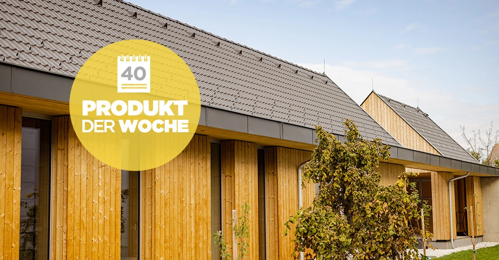 Gebäude mit Holzverkleidung steht still in einem Außenbereich mit Bäumen und Blauem Himmel. Gelber Kreis mit Schrift Produkt der Woche und Zahl 40 ist oben links abgebildet