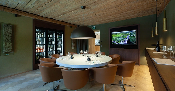 Galerie-Bild 5: Runder Tisch steht in der Mitte eines stilvollen Raumes umgeben von braunen Stühlen Gläser und Karaffen darauf an der Wand ein großer Bildschirm und im Hintergrund ein Weinschrank.