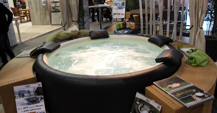 Galerie-Bild 27: Runder Whirlpool läuft in einer Messeumgebung umgeben von Kissen Prospekten und Handtüchern Text auf Schildern Bis zu 40°C warmes Wasser zu jeder Jahreszeit www.softub.at Ideal für Garten und Dach