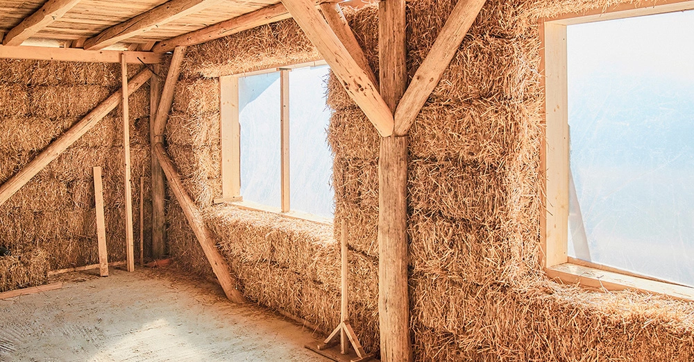 Strohhaus im Rohbau: Innenwände aus Holzständerbauweise mit Stroh ausgestopft. Helle große Fensteröffnungen. 