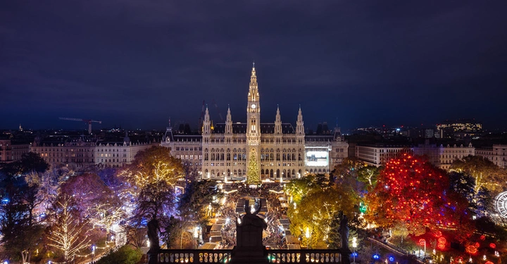 Panorama-Luftaufnahme des Wiener Christkindlmarkts am Rathausplatz mit beleuchtetem Rathaus, großem Weihnachtsbaum und Herzerlbaum.