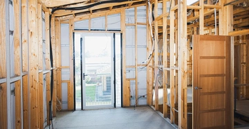 Holzrahmenstrukturen stehen in einem Raum im Bauprozess Innenansicht mit einem geöffneten Holztür und einem Glas-Schiebetür davor offener Rahmen mit sichtbaren Drähten und Isolierung im Bauumfeld