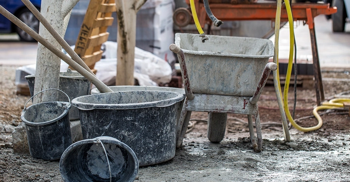 Symbolbild zum Thema Baukosten: Eine unaufgeräumte Baustelle mit einer schmutzigen Schubkarre und Mörtelkübeln, die die anfallenden Kosten bei einem Neubau repräsentieren.