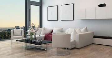 Ein modernes Wohnzimmer zeigt weiße Möbel wie Sofas und Stühle, einen niedrigen schwarzen Tisch mit Blumen und Dekoration, große Fenster, hellen Holzboden und zwei minimalistische Bilder an der Wand.