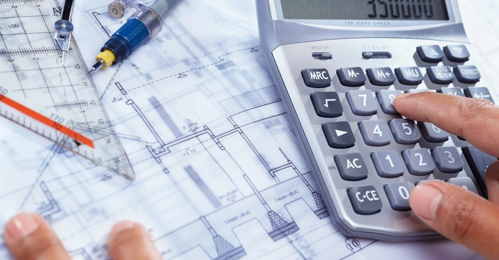 Männerhand tippt Zahlen in Taschenrechner (350.000), Plan mit Zirkel, Kugelschreiber und Dreieck-Lineal