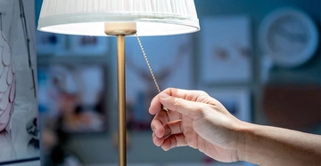 Männliche Hand zieht an der Kette eines Lichtschalters an einer weißen Lampe in einem Einrichtungsgeschäft.