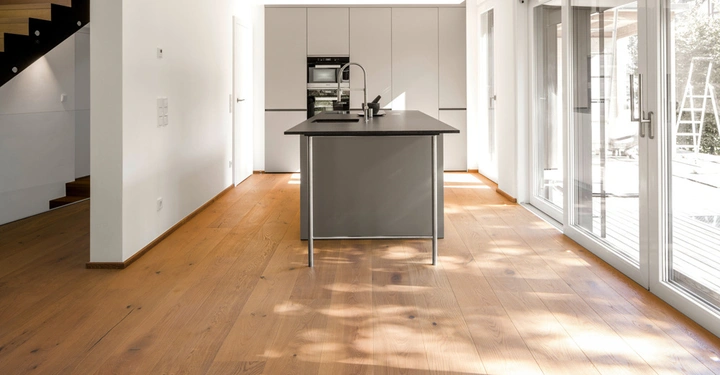 Kücheninsel steht in modernem Raum mit Holzfußboden großen Glasfenstern und einer Treppe zur linken Seite.