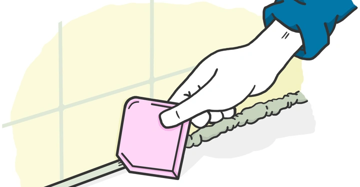 Hand hält ein rosa Werkzeug während des Abziehens von überschüssigem Dichtungsmittel auf Fliesen in einem Badezimmer