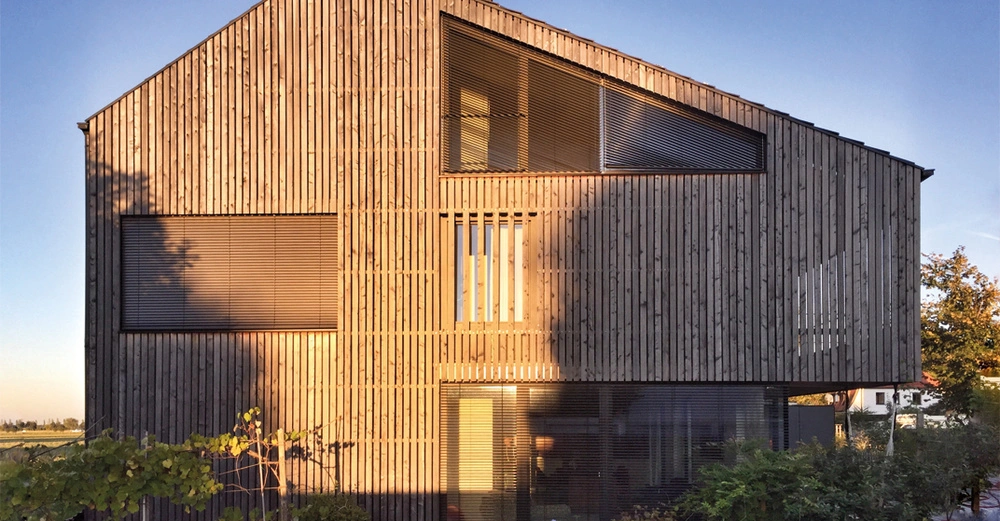wunderschönes, sonnenbeschienenes Holzhaus mit Lamellenfassade vor blauem Himmel