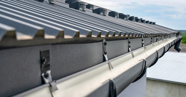 Nahaufnahme einer modernen, weißen halbrunden Regenrinne aus Metall, befestigt an einem Metalldach mit Schneefanggittern.