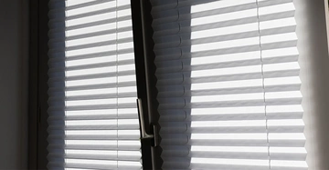 Gekipptes Fenster mit heruntergelassenem Plissee. Moderner Sicht- und Sonnenschutz im Wohnraum.