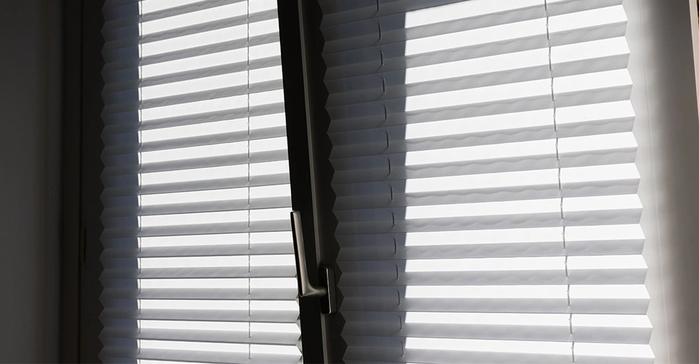 Gekipptes Fenster mit heruntergelassenem Plissee. Moderner Sicht- und Sonnenschutz im Wohnraum.