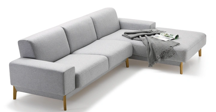 Galerie-Bild 1: Graues Ecksofa mit Holzbeinen liegt eine gefaltete graue Decke und zwei aufgeschlagene Magazine auf dem Abschnitt im Wohnzimmer.