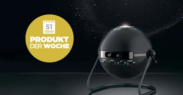 Schwarzer kugelförmiger Projektor projiziert Sterne auf dunklen Hintergrund. Stehend auf dreibeinigem Gestell in einem dunklen Raum. Text auf gelbem Kreis: 51 PRODUKT DER WOCHE