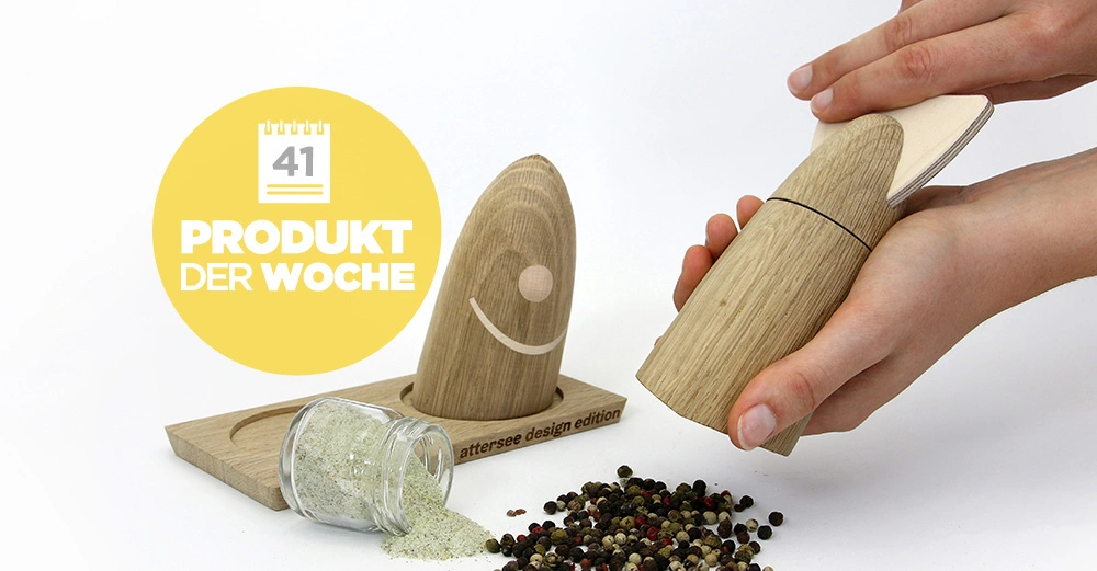 Hölzerner Pfeffermühlen-Set auf Tisch Hände mahlen Pfefferkörner daneben leeres umgekipptes Glas Text auf gelbem Hintergrund Produkt der Woche 41 attersee design edition