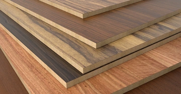 Mehrere Holzplatten mit verschiedenen Farben und Maserungen sind aufeinander gestapelt in einem Stapel. Die Umgebung besteht aus glatten Holzoberflächen.