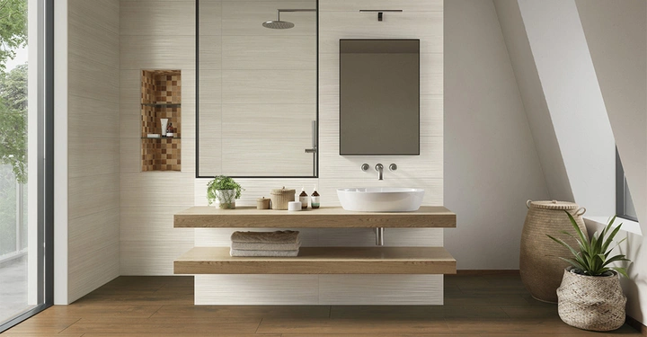 Waschbecken auf Holzarbeitsplatte steht im modernen Badezimmer mit Naturfarben Spiegel und Pflanzen in Körben daneben große Fenster zeigen grüne Bäume draußen.