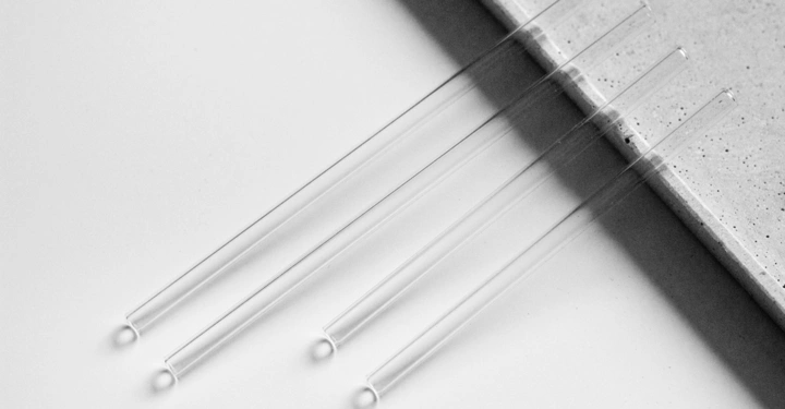 Drei transparente Glasröhrchen liegen nebeneinander auf einer weißen Oberfläche neben einer grauen, strukturierten Kante.