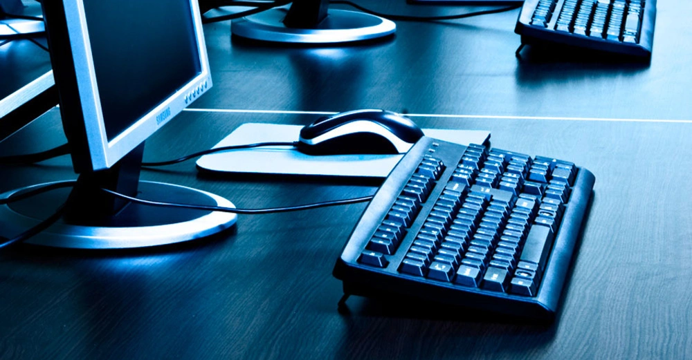 Mehrere Computerbildschirme stehen auf einem schwarzen Tisch in einem gut beleuchteten Raum mit Tastaturen und Mäusen davor in einer aufgeräumten Anordnung.