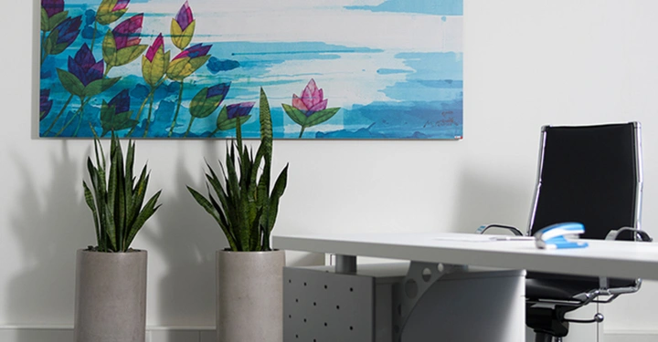 Galerie-Bild 1: Zwei Topfpflanzen stehen neben einem modernen, weißen Schreibtisch mit einem schwarzen Bürostuhl, eingerahmt durch ein buntes Wandbild mit Blumenmotiven an der weißen Wand im Hintergrund.