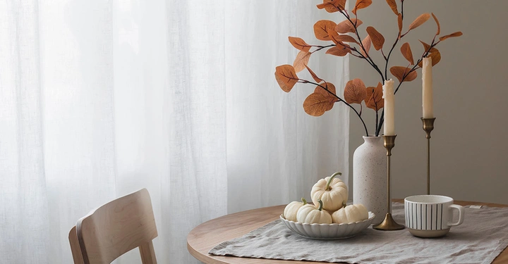 Weiße kleine Kürbisse, Kerzen und eine braune Pflanze auf einem Tisch. Herbstdekoration für Zuhause. 