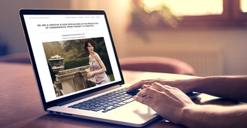 Ein Laptop zeigt eine Webseite über ein Kreativstudio für Cinemagraphs person tippt darauf helle häusliche Umgebung. Text: WE ARE A CREATIVE STUDIO SPECIALIZING IN THE PRODUCTION OF CINEMAGRAPHS FROM CONCEPT TO CREATION CINEMAGRAPHS FROM PROSPEKT 2017.