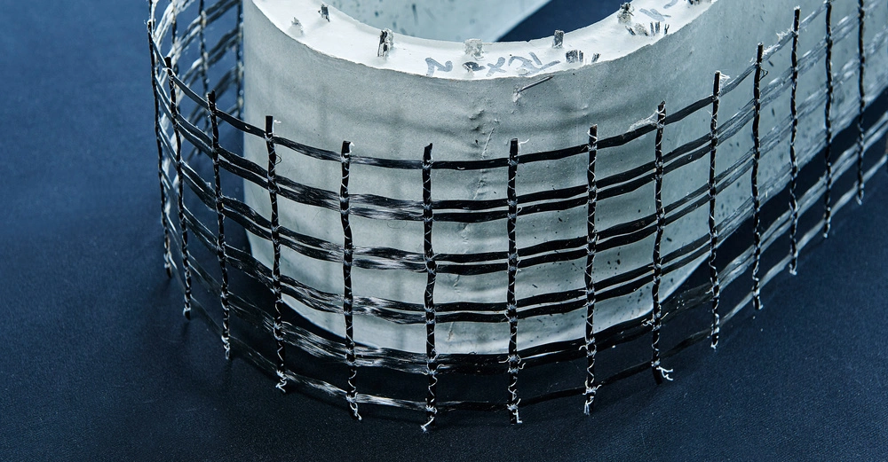 Stahlgitter umwickelt einen gebogenen Betonstrukturblock auf einem dunklen Hintergrund. Auf dem Beton stehen die Zahlen 232.