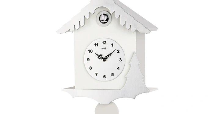 Galerie-Bild 11: Eine weiße Kuckucksuhr zeigt 10 Uhr. Oben ragt ein Kuckuck heraus. Die Uhr hängt in einem schlichten Raum. Beschriftung auf dem Zifferblatt AMS.