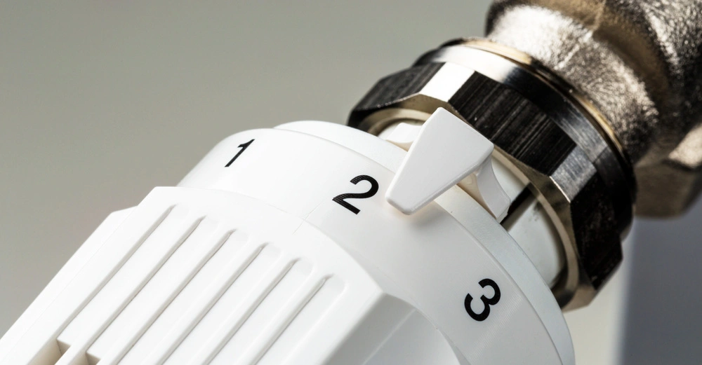 Weißer Heizungsregler-Einstellen Stufen 1 bis 3 auf Metallrohr montiert Vor grauem Hintergrund