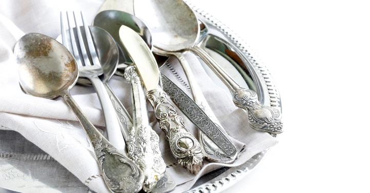 Tablett mit weißer Stoffserviette auf der einige Messer, Gabeln und Löffel aus echtem Silber liegen. Löffel bereits angelaufen.