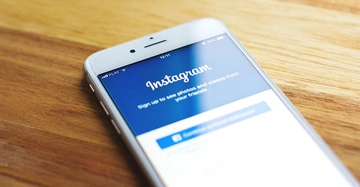 Smartphone liegt auf einem Holztisch zeigt Instagrams Anmeldebildschirm. Text: Instagram Sign up to see photos and videos from your friends.