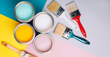 Dosen mit türkisgelber rosa und weißer Farbe stehen offen Farbpinsel liegen daneben der Hintergrund ist einfarbig pastellgelb türkis rosa und grau.