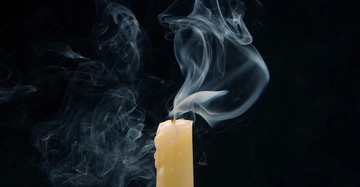 Eine weiße Kerze erlischt vor schwarzen Hintergrund.