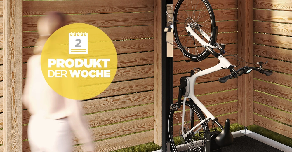 Ein Fahrrad steht vertikal an einem Ständer innerhalb eines Holzschuppens. Ein unscharfer Mensch geht vorbei. Text: 2 Produkt der Woche.
