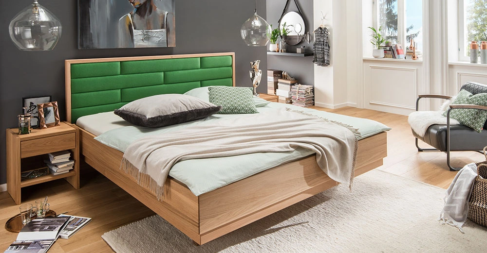 Ein Bett mit grünem Kopfteil steht in einem modernen Schlafzimmer mit Holzboden und grauer Wand; Tagesdecke ist beigefarben, zwei Kissen sind grau und grün gemustert. Rug.